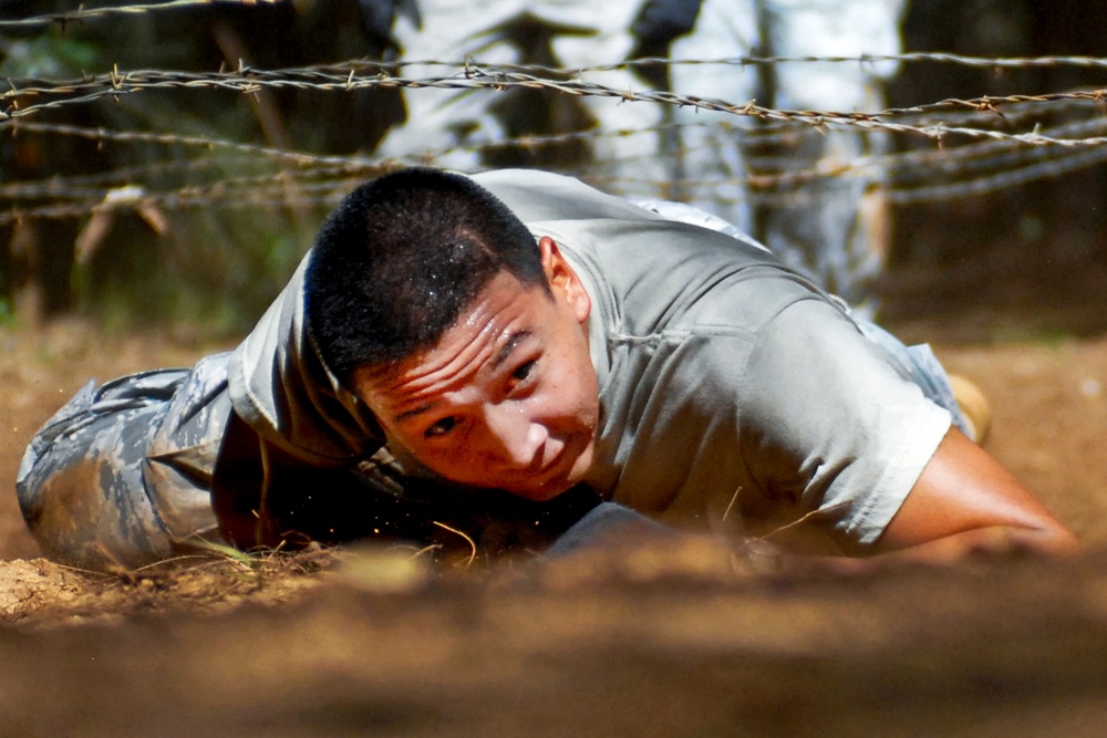Senior Airman Anthony Elizondo low crawls under barbed wire as part of an obstacle course.