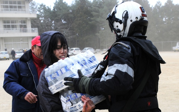 Petty Officer 2nd Class Zack DelCorte hands bottled water to a Japanese citizen.