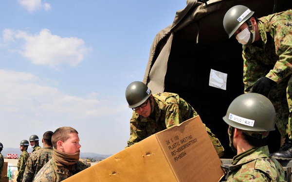 A U.S. Marine and Japanese Ground Self-Defense Force soldiers load boxes of donated blankets and clothing.