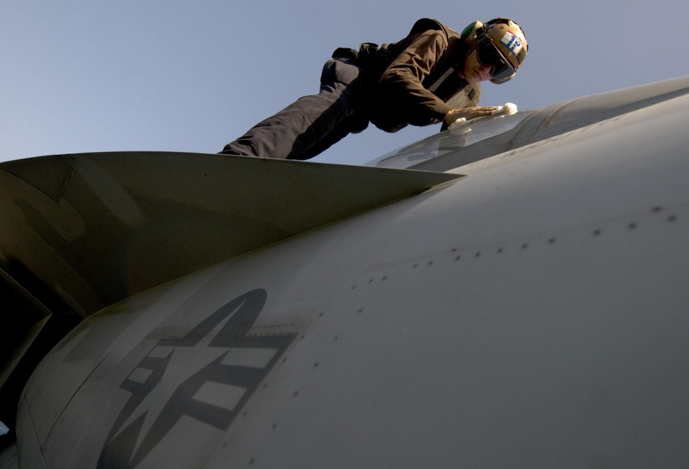 Seaman Bryan Domingue cleans the canopy on an F/A-18F Super Hornet aircraft