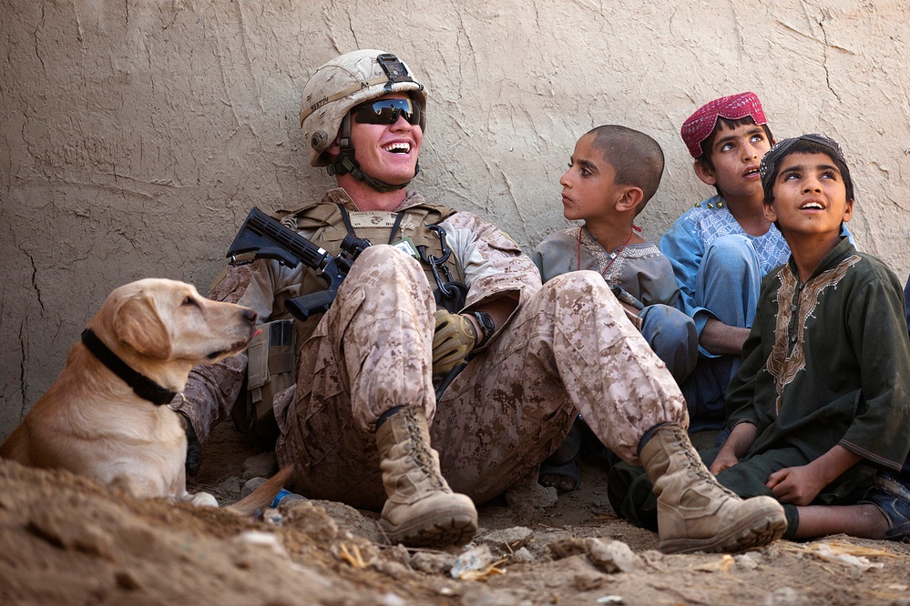 Lance Cpl. Isaiah Schult jokes with Afghan children and an Afghan National Police officer outside a local residence.