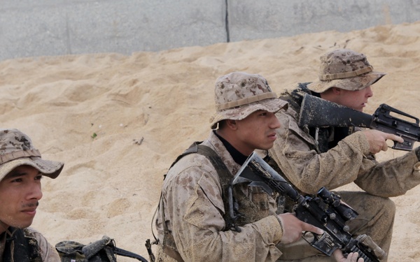 Marine scout swimmers kneel as they provide security on a beach.