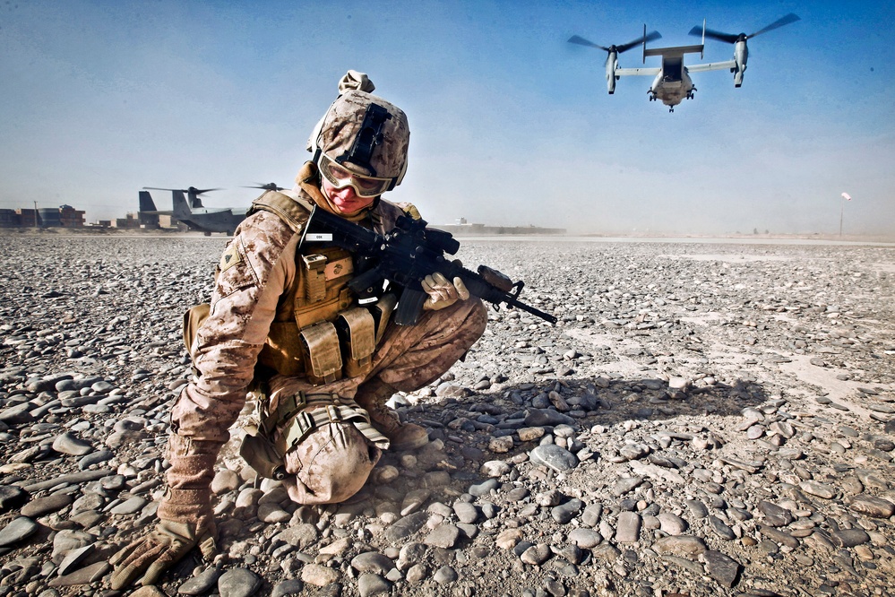 Cpl. William Cox shields himself from flying rocks and sand as an MV-22 Osprey aircraft prepares to take off.