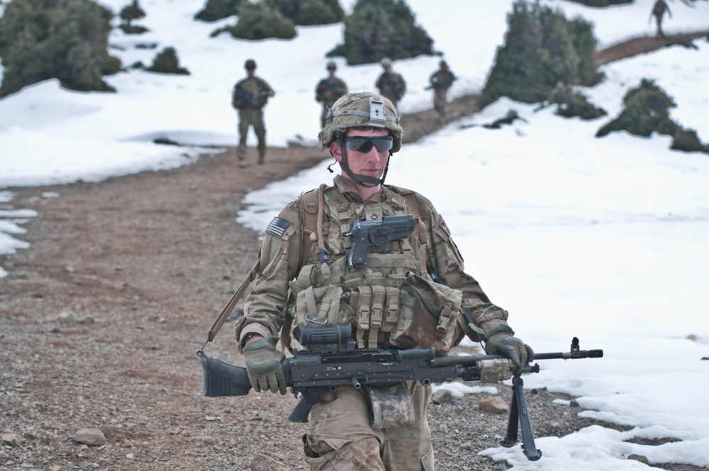 Pfc. Cristian Franco carries an M240B machine gun while descending a mountain path.