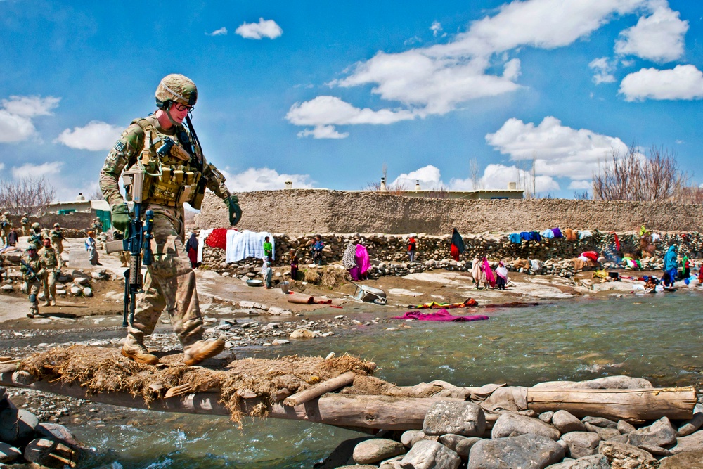 U.S. Army Sgt. Michael Trevino uses a foot bridge to cross a swollen river.