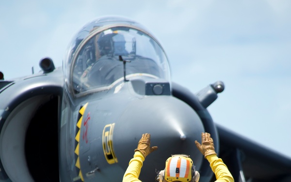 A flight deck crewman directs the pilot of an AV-8B Harrier jet
