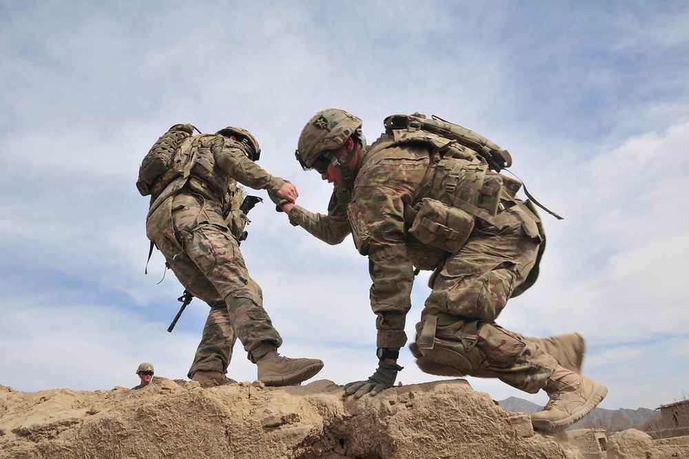 A soldier helps a fellow soldier onto the rooftop of an old building