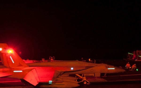 A U.S. Navy F/A-18F Super Hornet is prepared for a nighttime catapult launch