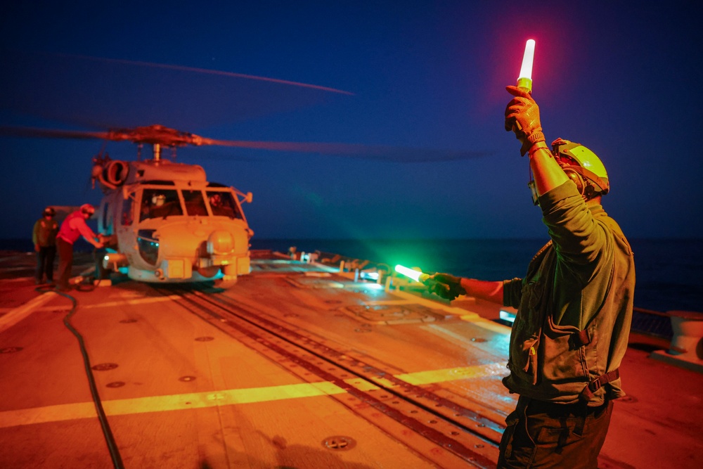 AD2 Keith Gonzales signals to MH-60R Sea Hawk helicopter pilots with illuminated batons