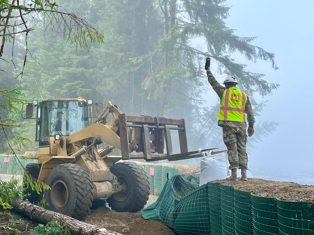 Command Sgt. Maj. Zachary Plummer assists the street team to repair a temporary flood protection barrier along the Mendenhall River