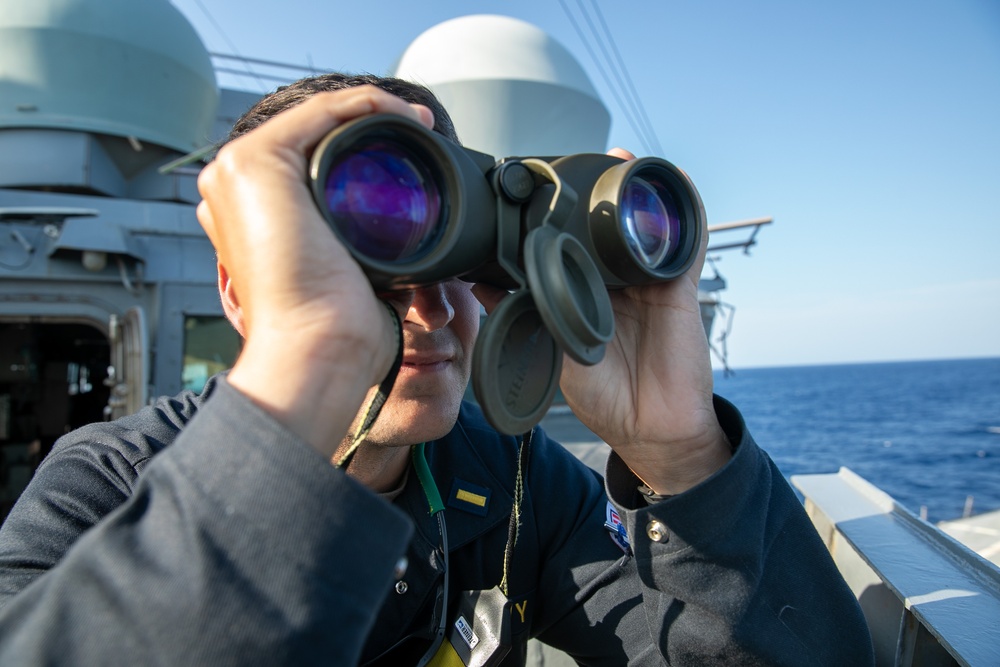 USS Mitscher (DDG 57) officer looks through binoculars on ship's bridge wing