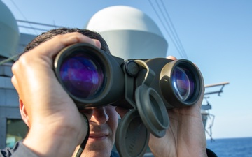USS Mitscher (DDG 57) officer looks through binoculars on ship's bridge wing