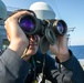 USS Mitscher (DDG 57) officer looks through binoculars on ship's bridge wing
