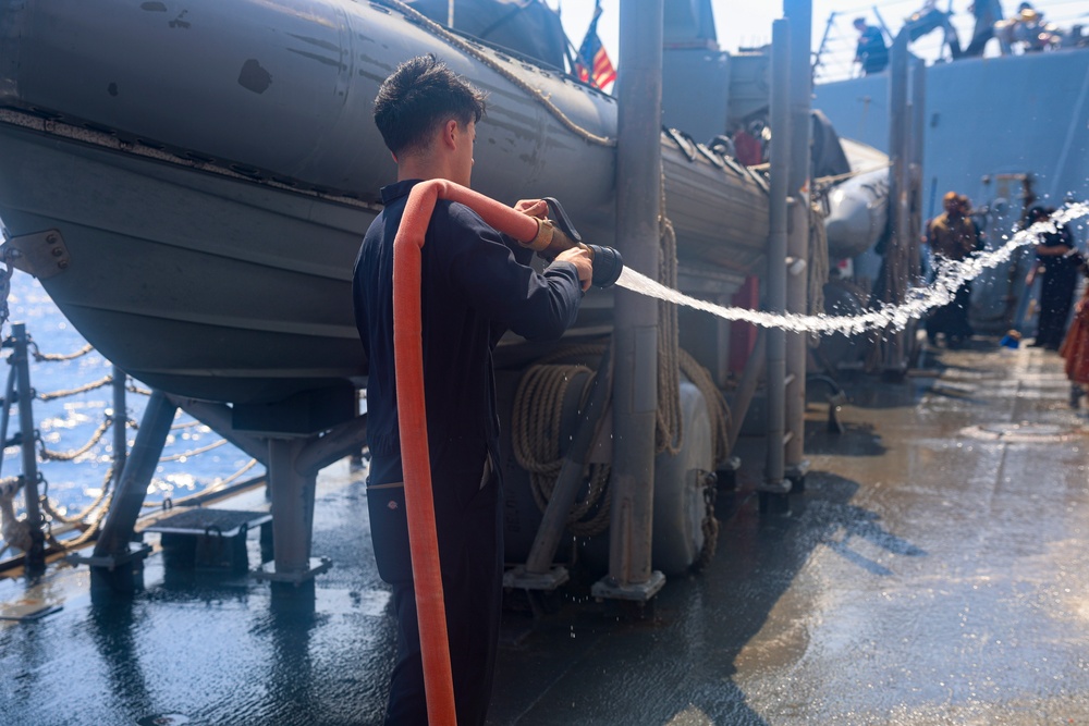 DCFN Eli Gavilanes operates a fire hose to clean exterior surfaces of the ship