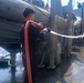 DCFN Eli Gavilanes operates a fire hose to clean exterior surfaces of the ship