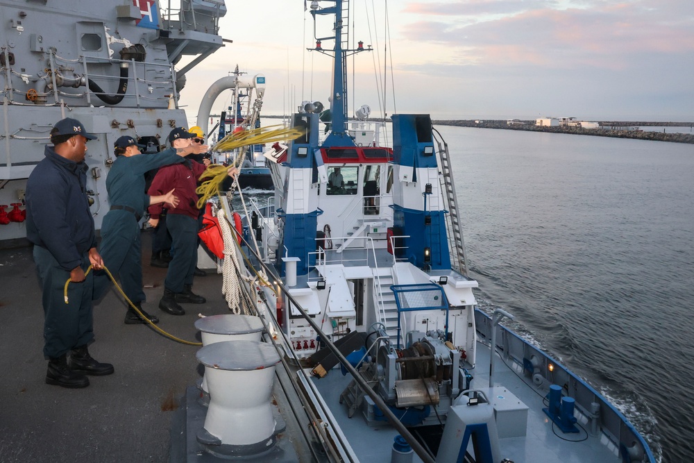 Sailors toss a mooring line to a tug boat during a sea-and-anchor