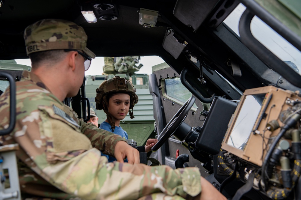 U.S. Army Soldier assists Polish boy trying on helmet inside military vehicle