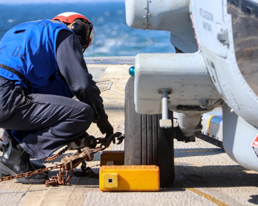 BM3 Carlens Milice removes the chocks and chains prior to an MH-60R Seahawk take-off during the Northern Coasts 2025