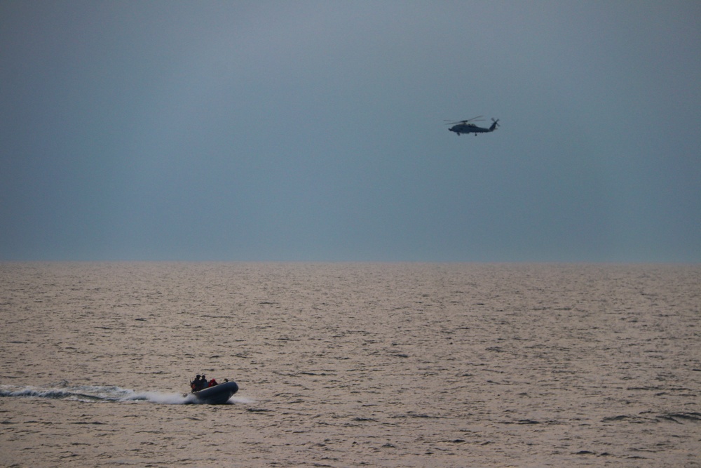 A MH-60R Sea Hawk helicopter conducts maneuvers alongside a rigid-hulled inflatable boat during exercise Northern Coasts 2025