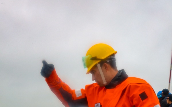 BM1 Jason Carpenter signals to coordinate with a tugboat line handler