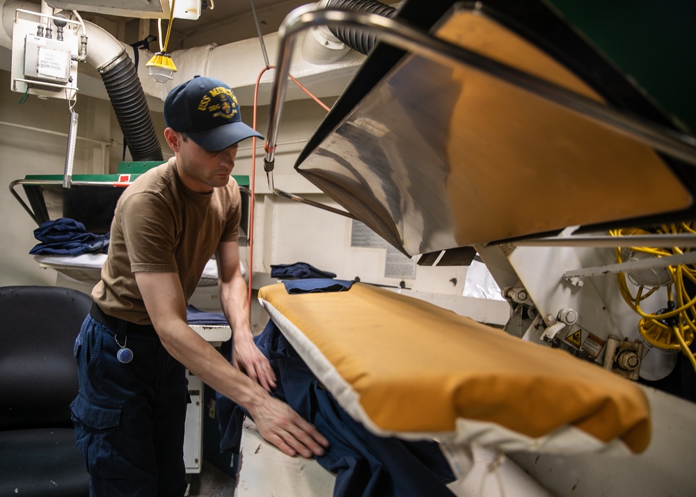USS Mitscher (DDG 57) Sailor presses uniforms in ships laundry
