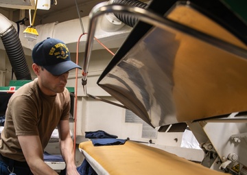 USS Mitscher (DDG 57) Sailor presses uniforms in ships laundry