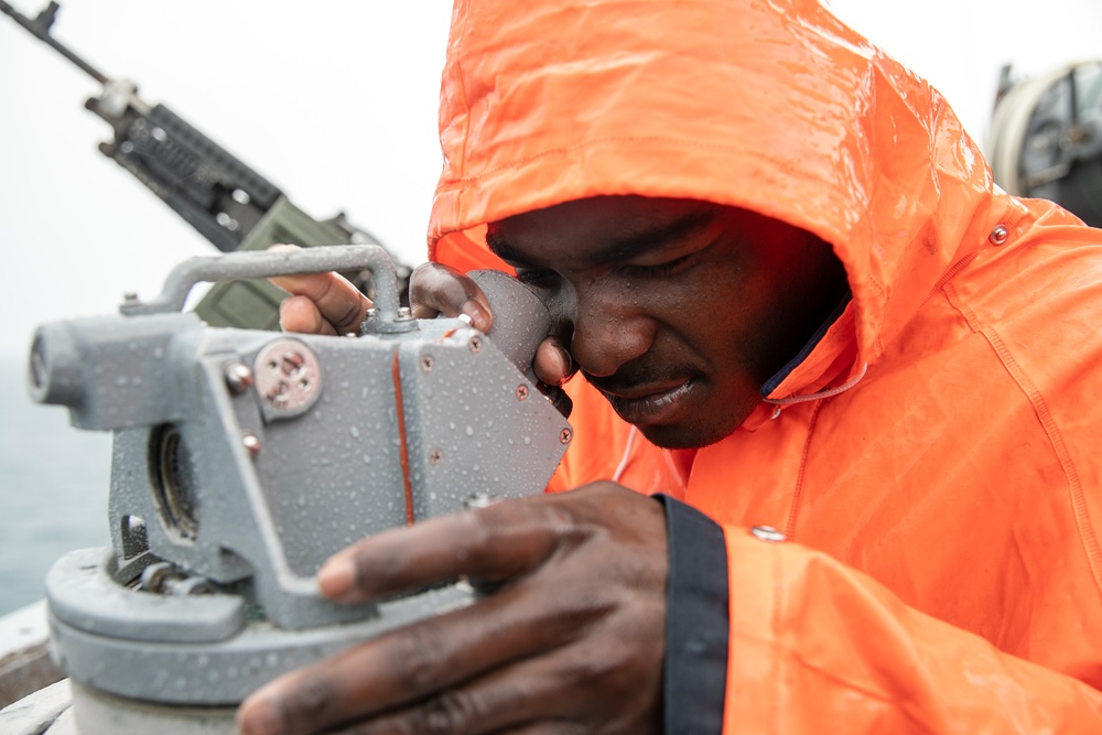USS Mitscher (DDG 57) Sailor looks through compass on bridge wing