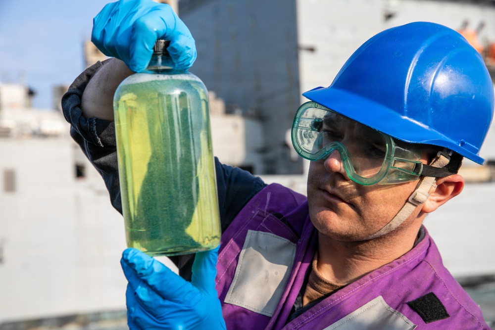 USS Mitscher (DDG 57) Sailor inspects fuel sample during RAS with USNS Carl Brashear (T-AKE 7)