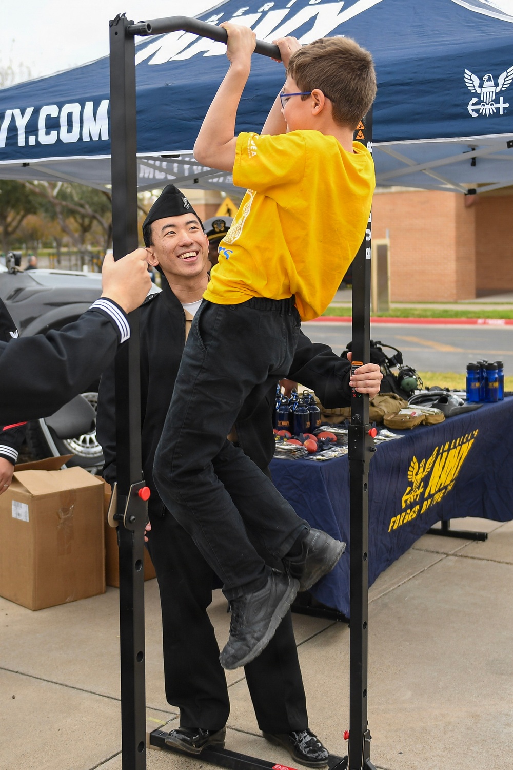 HM2 Ahn holds the pull up bar and watches as a civilian does pull ups