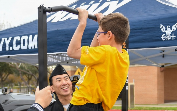 HM2 Ahn holds the pull up bar and watches as a civilian does pull ups