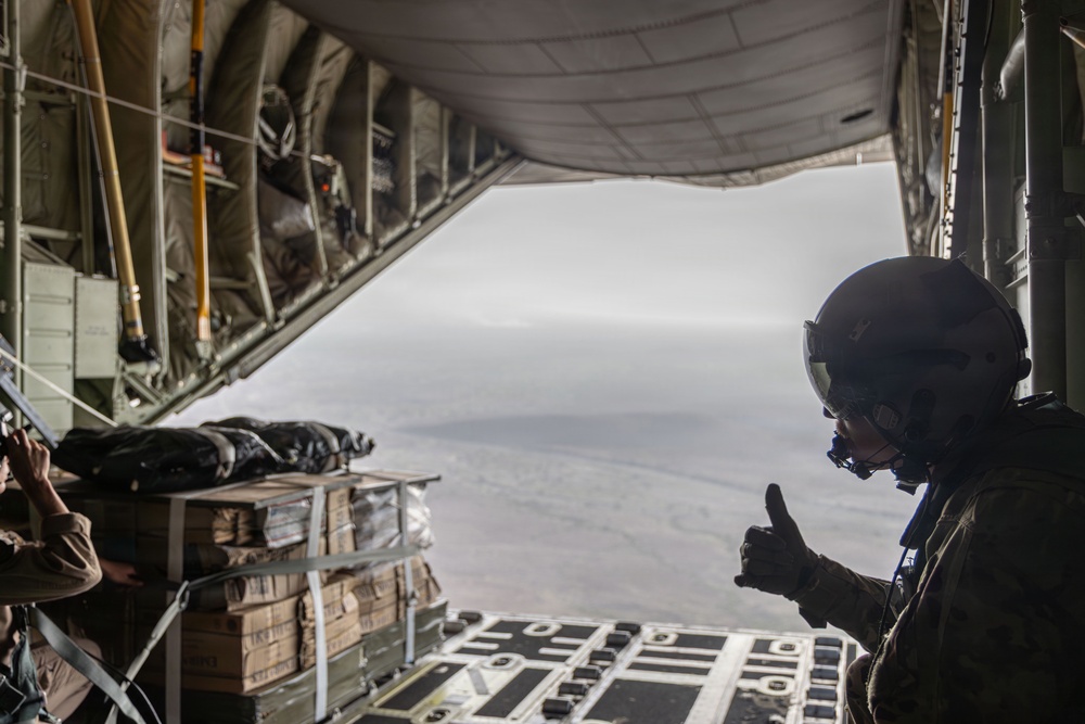 Air Force Loadmaster signals his team to drop cargo aboard a C-130 aircraft.