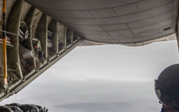 Air Force Loadmaster signals his team to drop cargo aboard a C-130 aircraft.