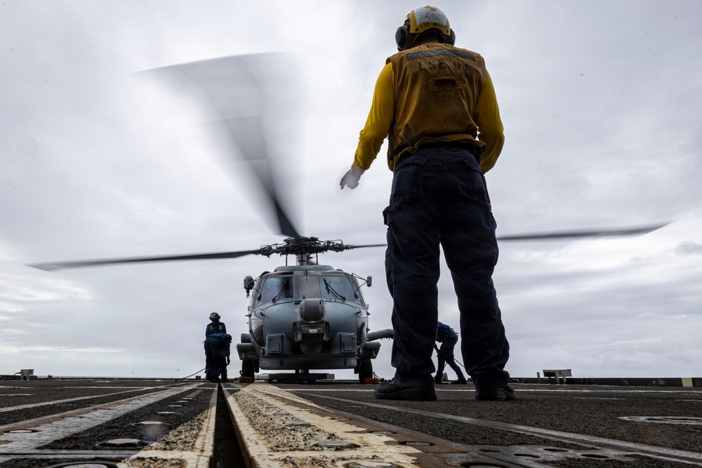U.S. Sailor signals Sailors to chock and chain an MH-60R Seahawk helicopter