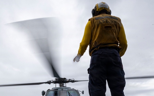 U.S. Sailor signals Sailors to chock and chain an MH-60R Seahawk helicopter
