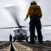 U.S. Sailor signals Sailors to chock and chain an MH-60R Seahawk helicopter