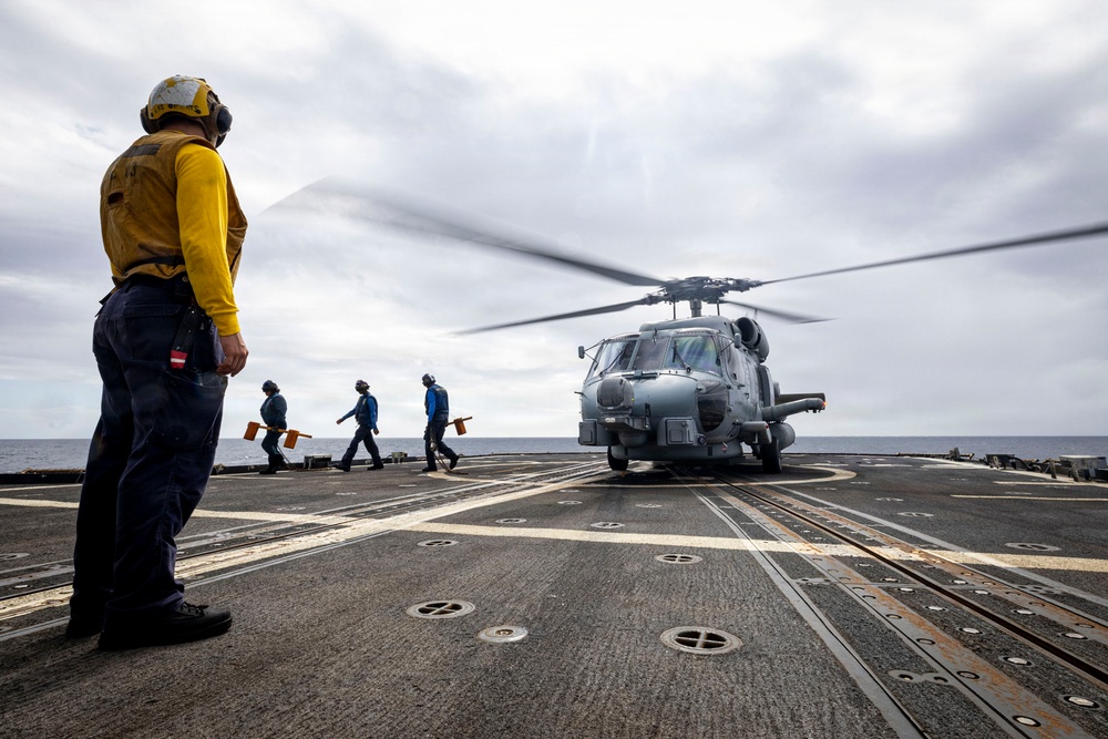 U.S. Sailor signals Sailors to remove chocks and chains from an MH-60R Seahawk helicopter