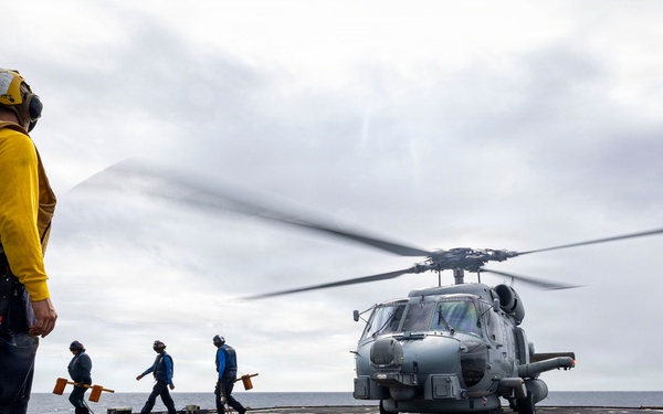 U.S. Sailor signals Sailors to remove chocks and chains from an MH-60R Seahawk helicopter