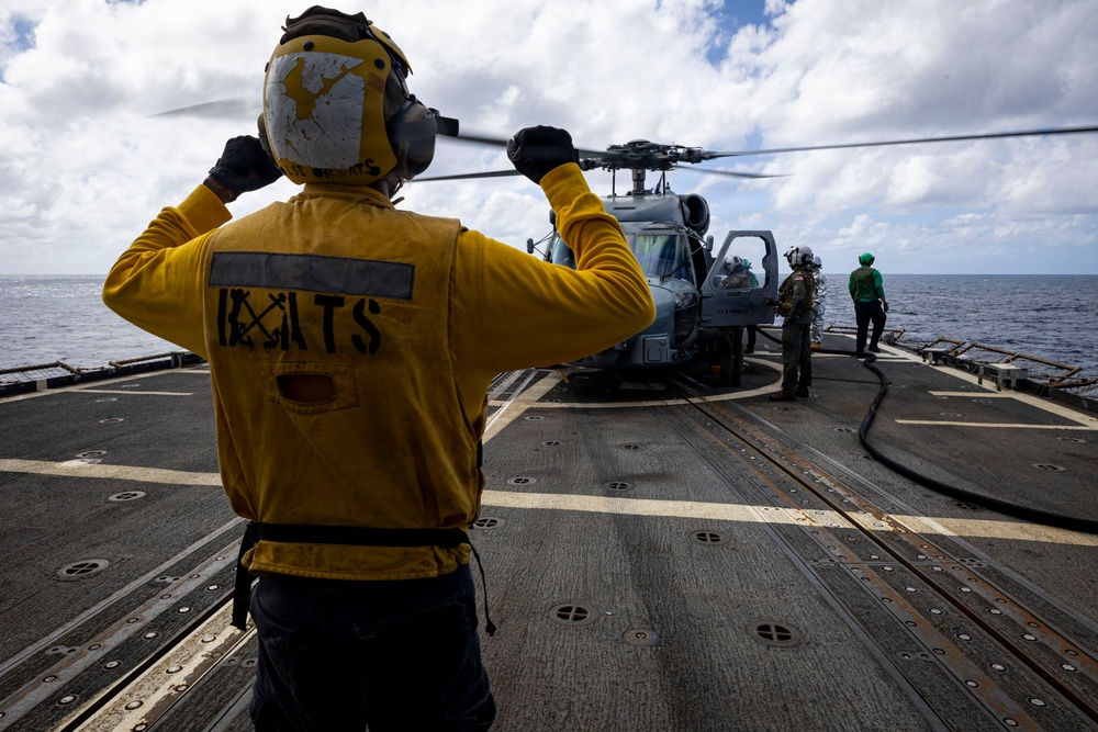 U.S. Sailor signals to flight deck crew near an MH-60R Seahawk helicopter on the flight deck
