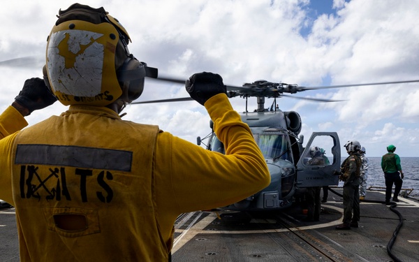 U.S. Sailor signals to flight deck crew near an MH-60R Seahawk helicopter on the flight deck