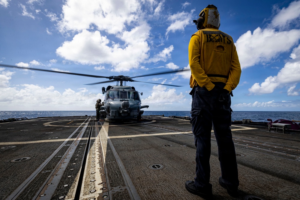 U.S. Sailor waits to signal an MH-60R Seahawk helicopter to lift off from the flight deck