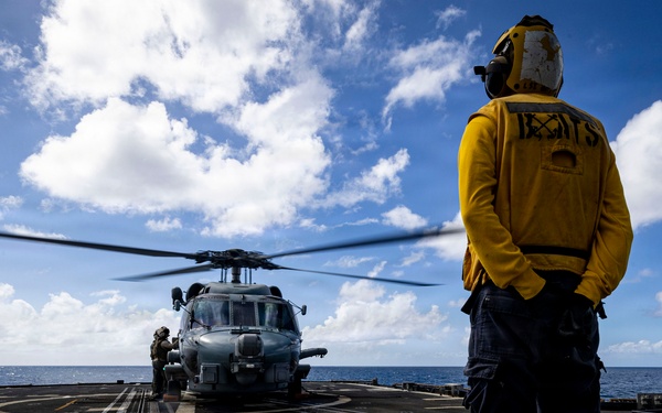 U.S. Sailor waits to signal an MH-60R Seahawk helicopter to lift off from the flight deck