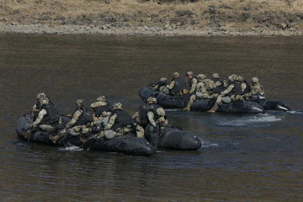 Soldiers paddle Zodiac boats across the river