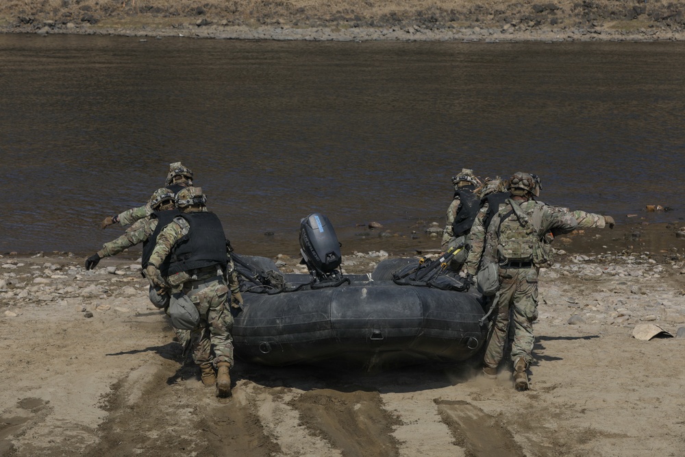 Soldiers carry a Zodiac boat towards a river