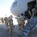 Military personnel in OCP (Operational Camouflage Pattern) uniforms are boarding a large military transport aircraft marked '0044' belonging to the 445th Airlift Wing (445th AW). Soldiers carrying rucksacks and personal gear are queued on the tarmac and ascending the boarding stairs into the aircraft. The scene appears to be a deployment or troop movement operation at a military airfield.