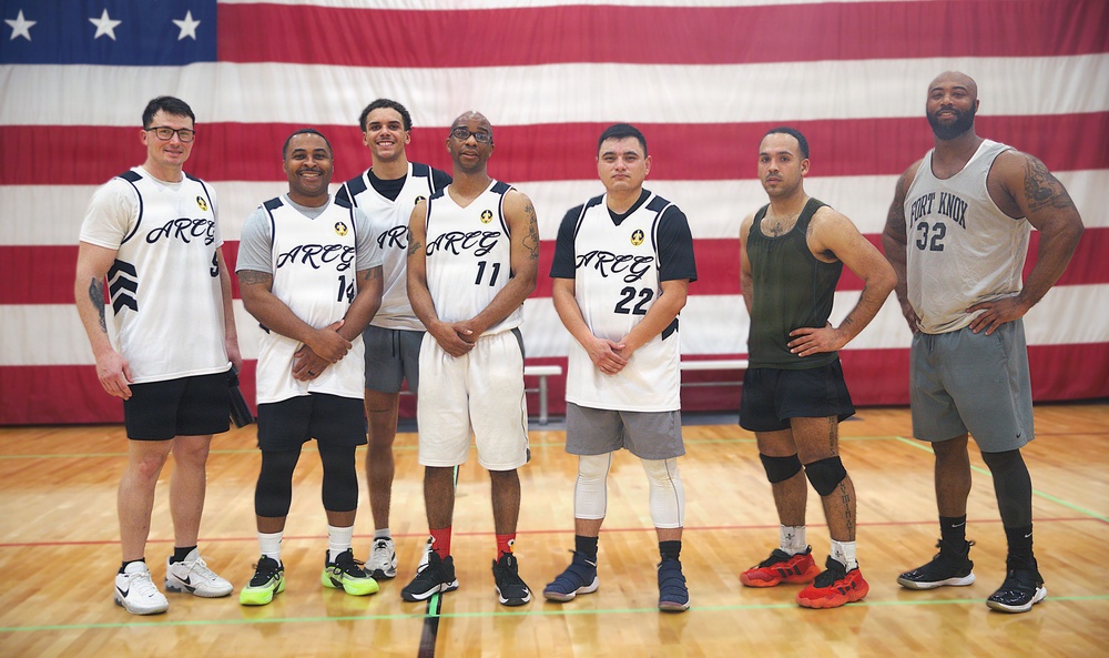 Army Reserve basketball team poses for group photo in front of American flag at Fort Knox gymnasium