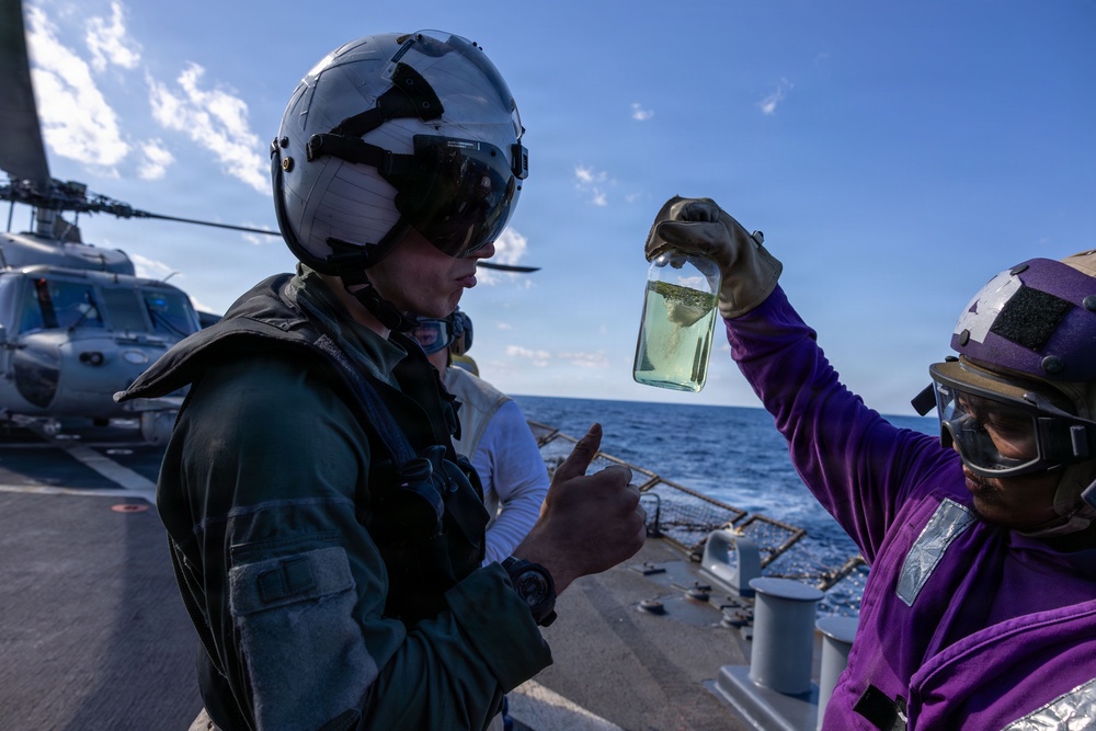 Sailors conduct fuel sample check prior to fueling a MH-60R Seahawk of HSM-46 on the USS Arleigh Burke