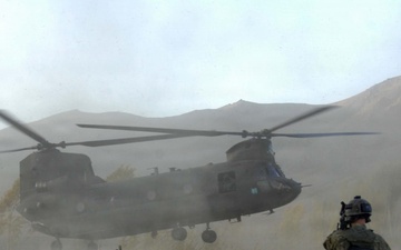 Soldiers brace themselves against the CH-47 Chinook helicopter rotor wash