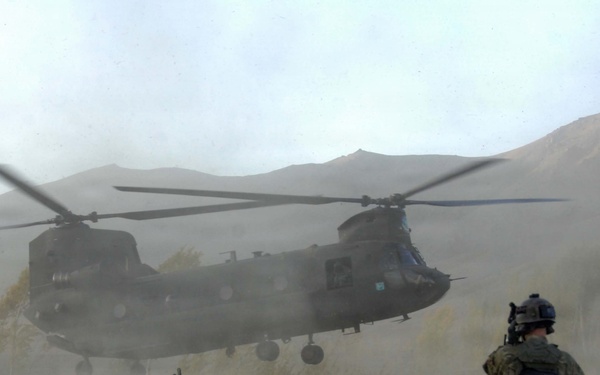 Soldiers brace themselves against the CH-47 Chinook helicopter rotor wash