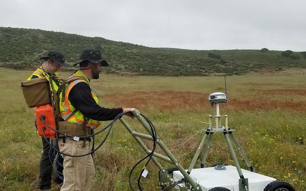 Technicians Operate Ground-Penetrating Radar Robot in Open Field During Unexploded Ordnance Survey
