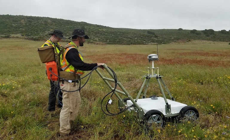 Technicians Operate Ground-Penetrating Radar Robot in Open Field During Unexploded Ordnance Survey